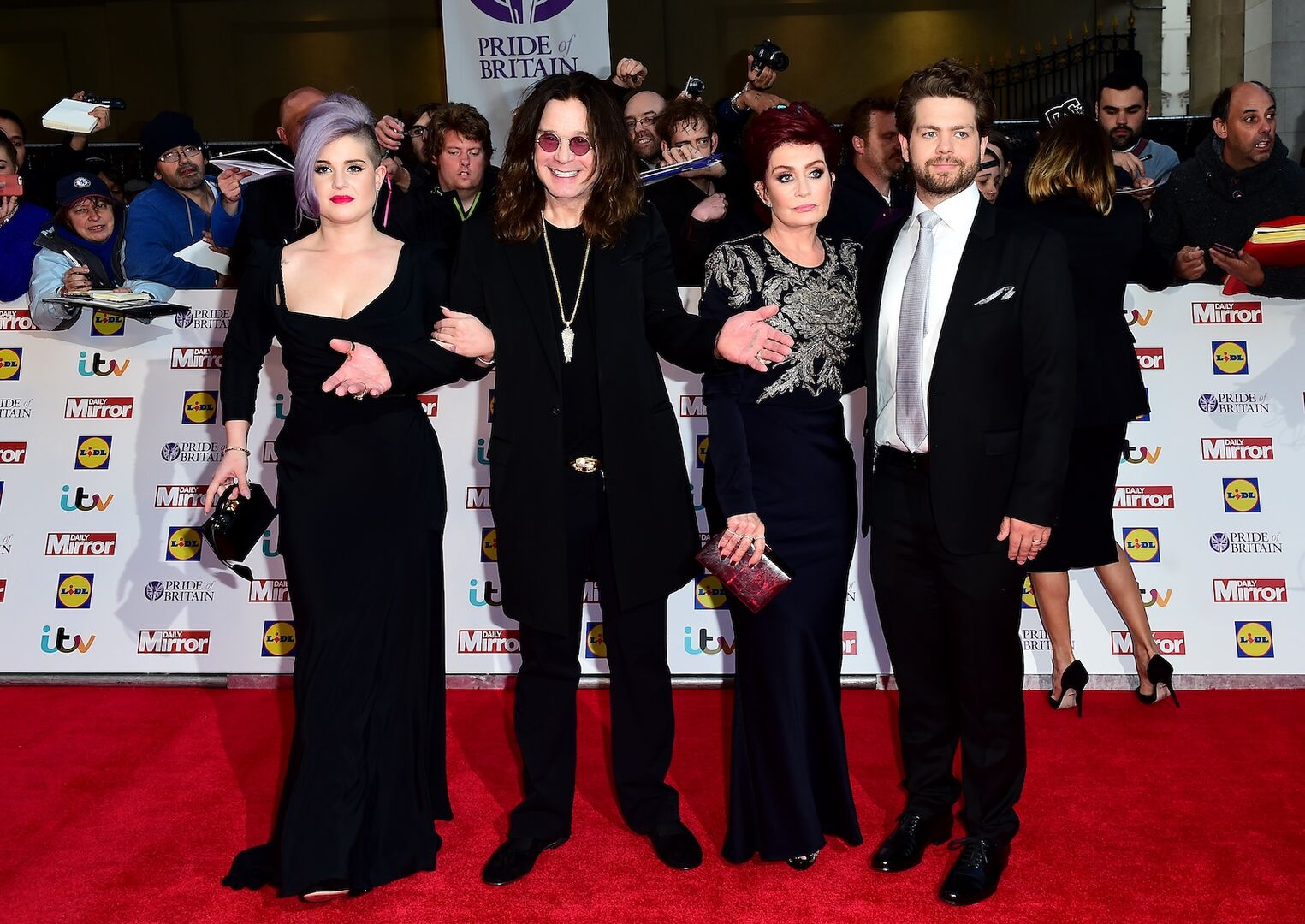 Kelly Osbourne, Ozzy Osbourne, Sharon Osbourne und Jack Osbourne posieren elegant gekleidet auf dem roten Teppich bei der „Pride of Britain“-Gala vor Fotowand und jubelnden Fans.