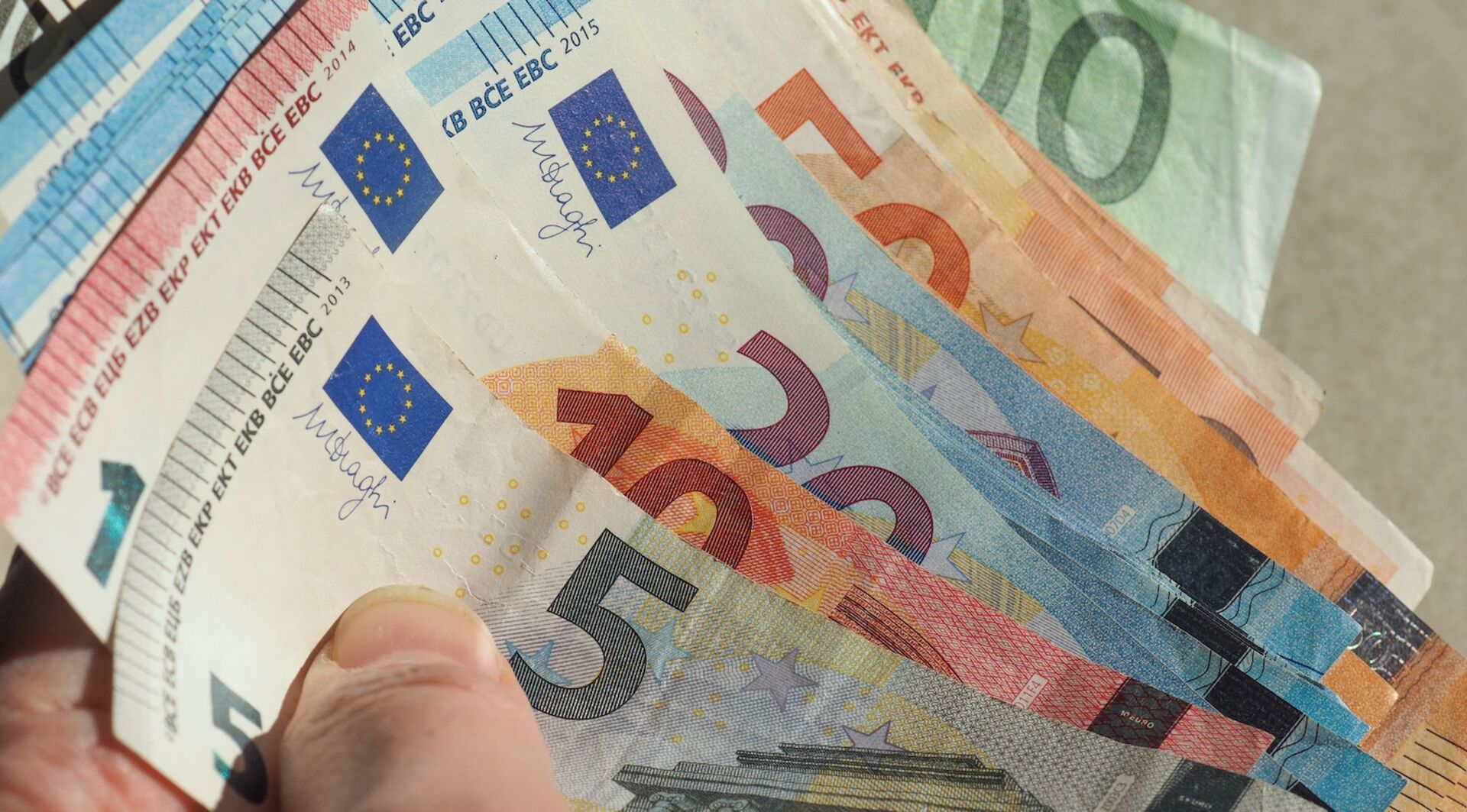 Hand hält aufgefächerte Euro-Banknoten in verschiedenen Stückelungen (5, 10, 20, 50, 100 Euro).