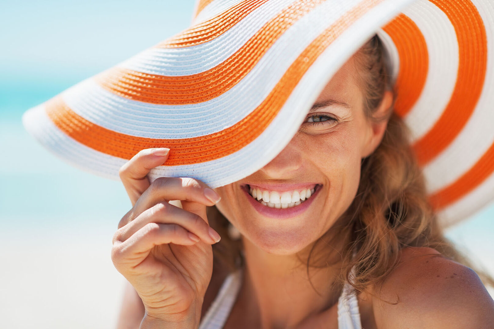 Frau mit Sonnenhut am Strand | Credit: iStock.com/CentralITAlliance