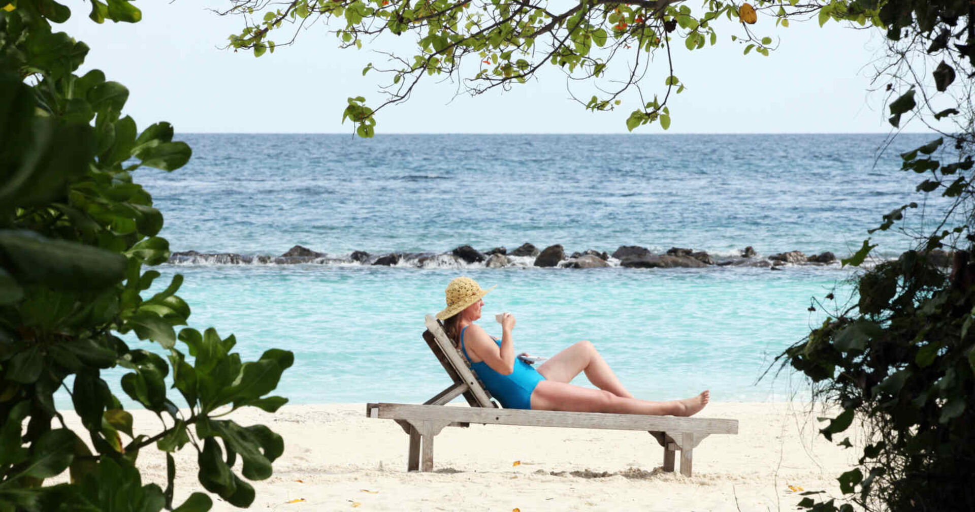 Frau im Badeanzug und mit Sonnenhut liegt auf einer Liege am Strand