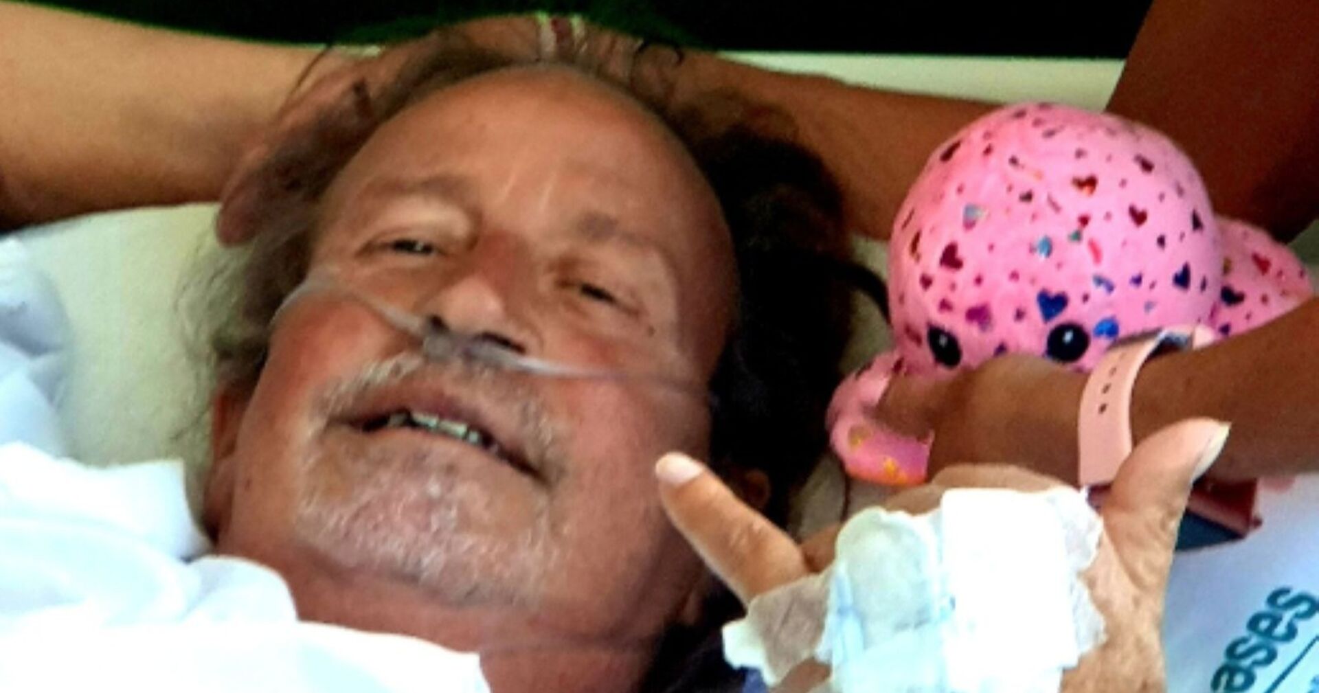 Thommy Schmelz liegt im Krankenhausbett und zeigt eine Coolness-signalisierende Handgeste