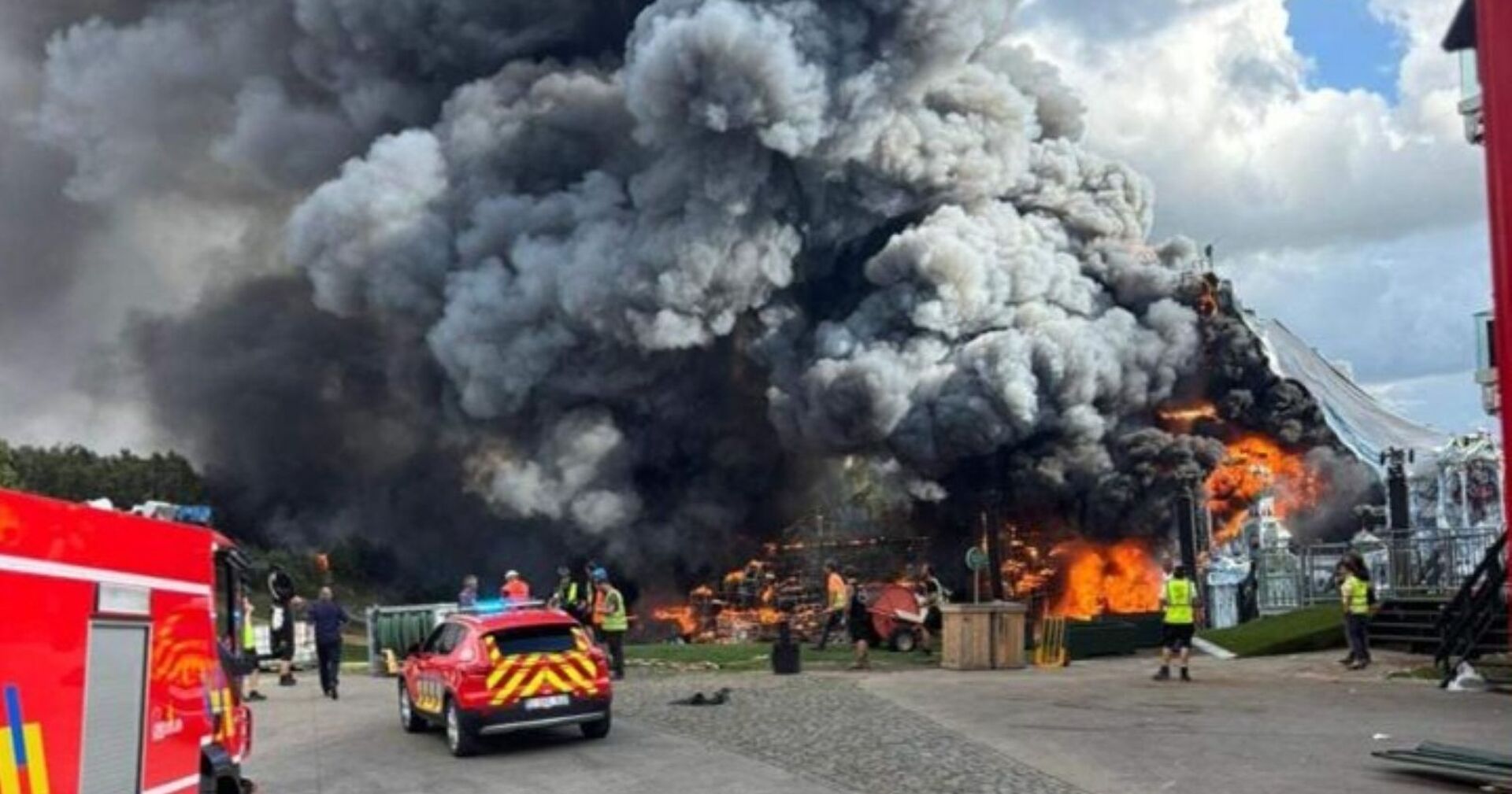 Großbrand auf dem Tomorrowland-Festivalgelände: Flammen und dichte schwarze Rauchwolken steigen über der zerstörten Mainstage auf, Feuerwehr und Einsatzkräfte sind vor Ort. L