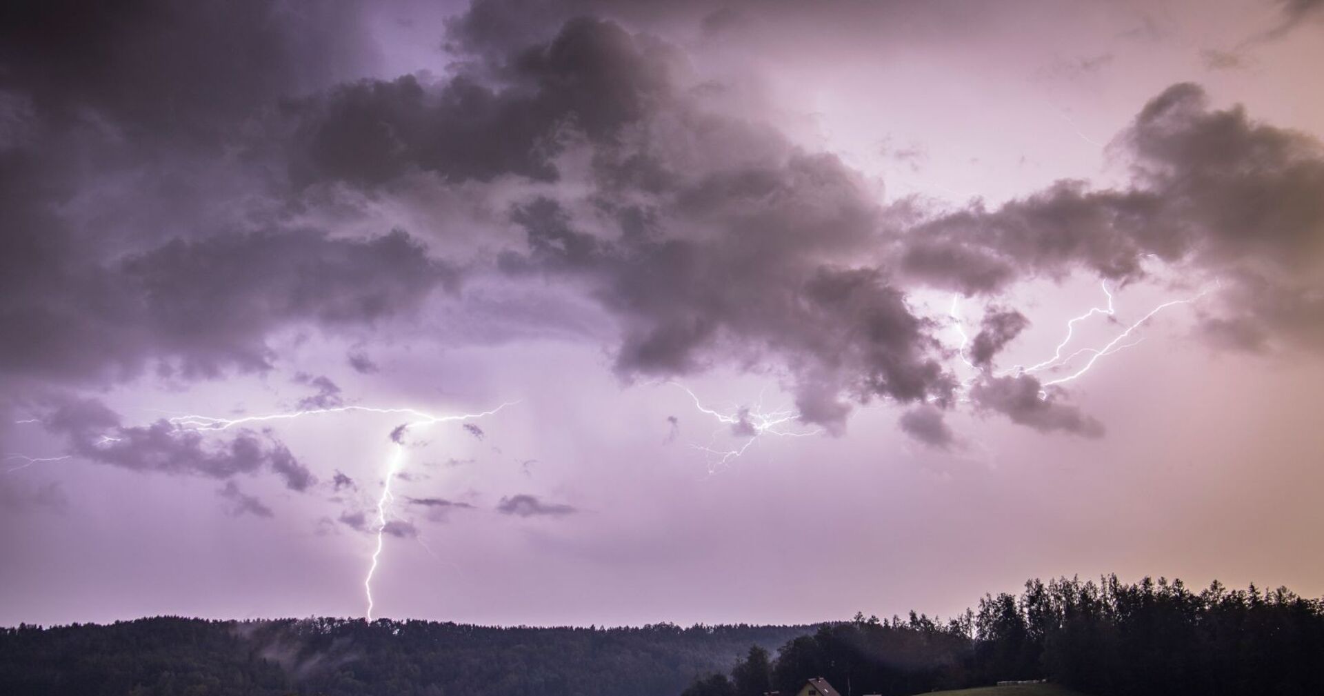 Gewitterfront mit dunklen Wolken und Blitzen über bewaldeter Landschaft