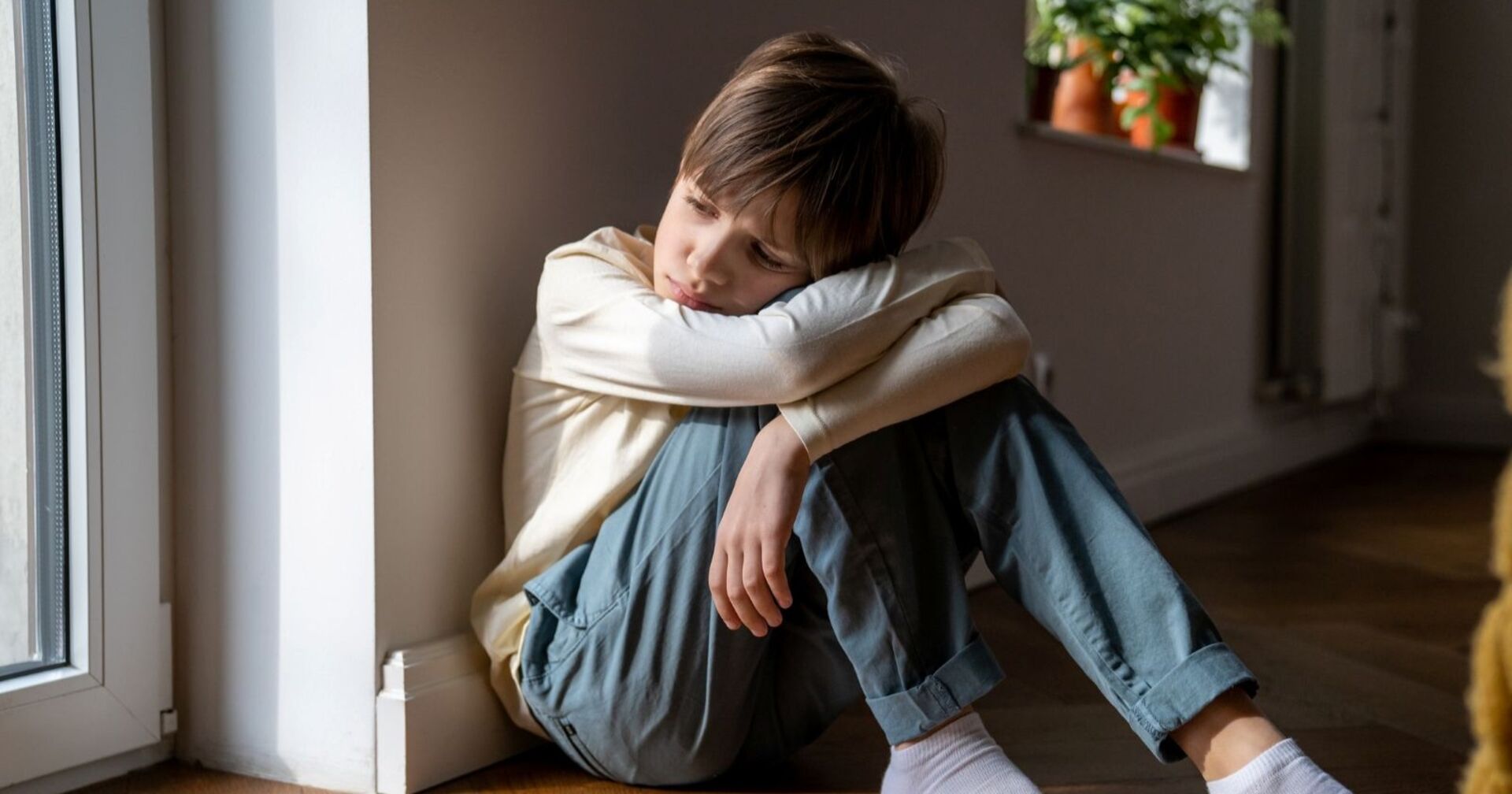 Junger Bub sitzt deprimiert an einem Fenster