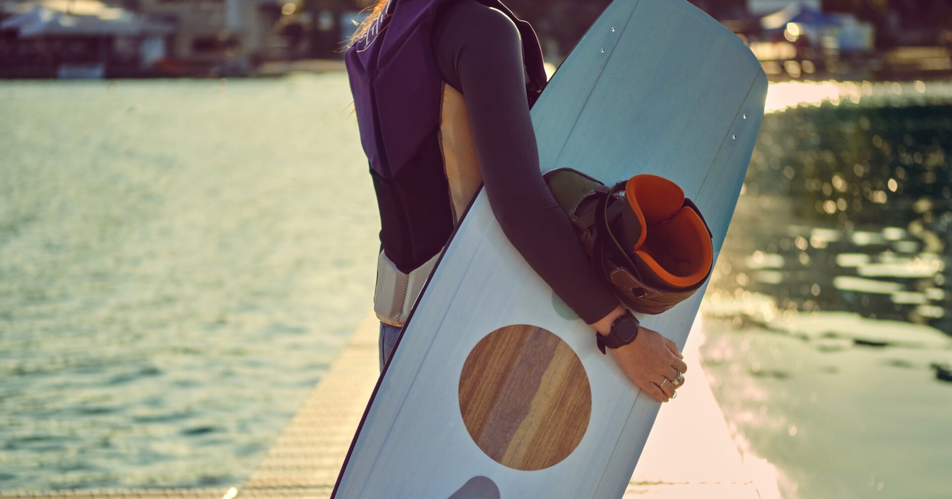 Ein Mädchen hält an einem See ein Wakeboard in der Hand.