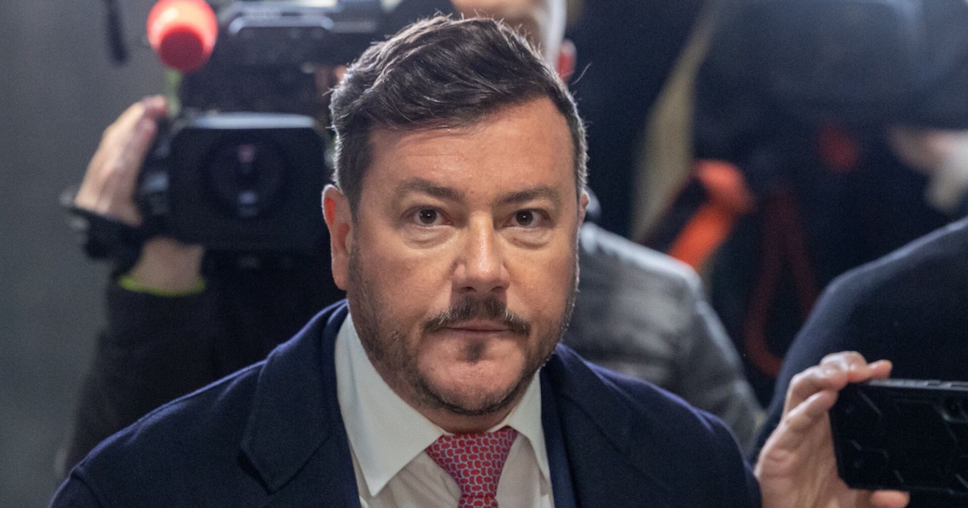 René Benko im Anzug und roter Krawatte vor Kameras und Journalisten