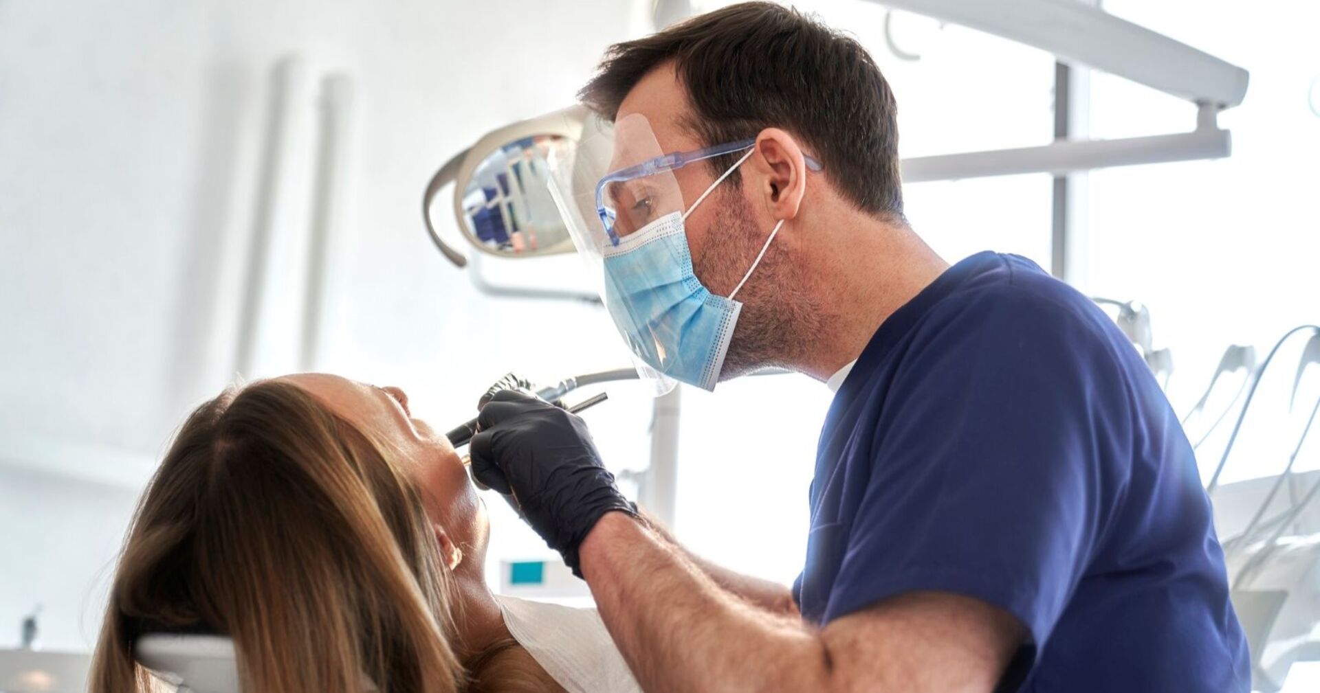 Zahnarztpraxis mit Arzt in blauer Kleidung und Patientin, die behandelt wird