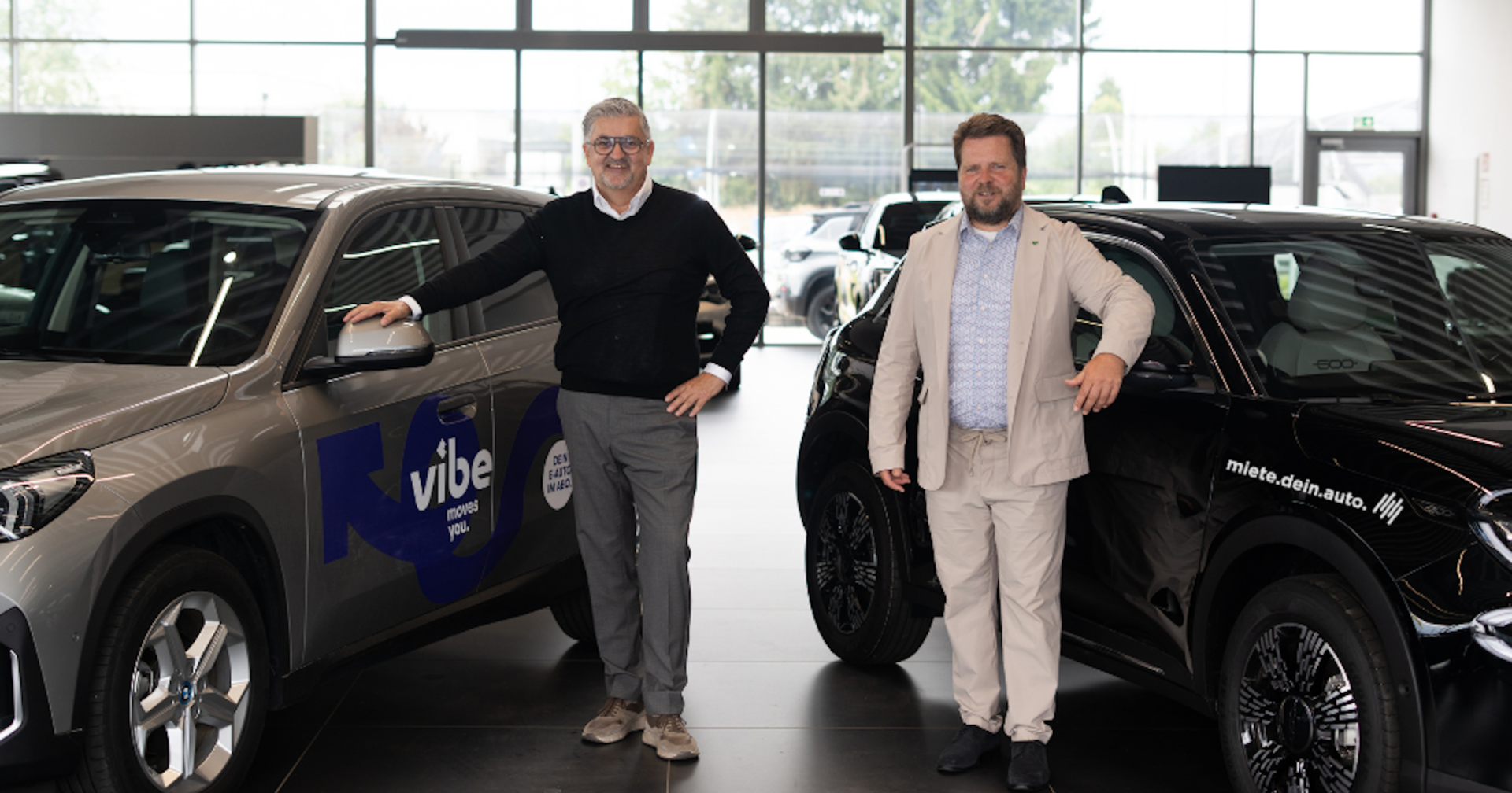 Porträt zweier Männer neben Autos stehend im Autohaus