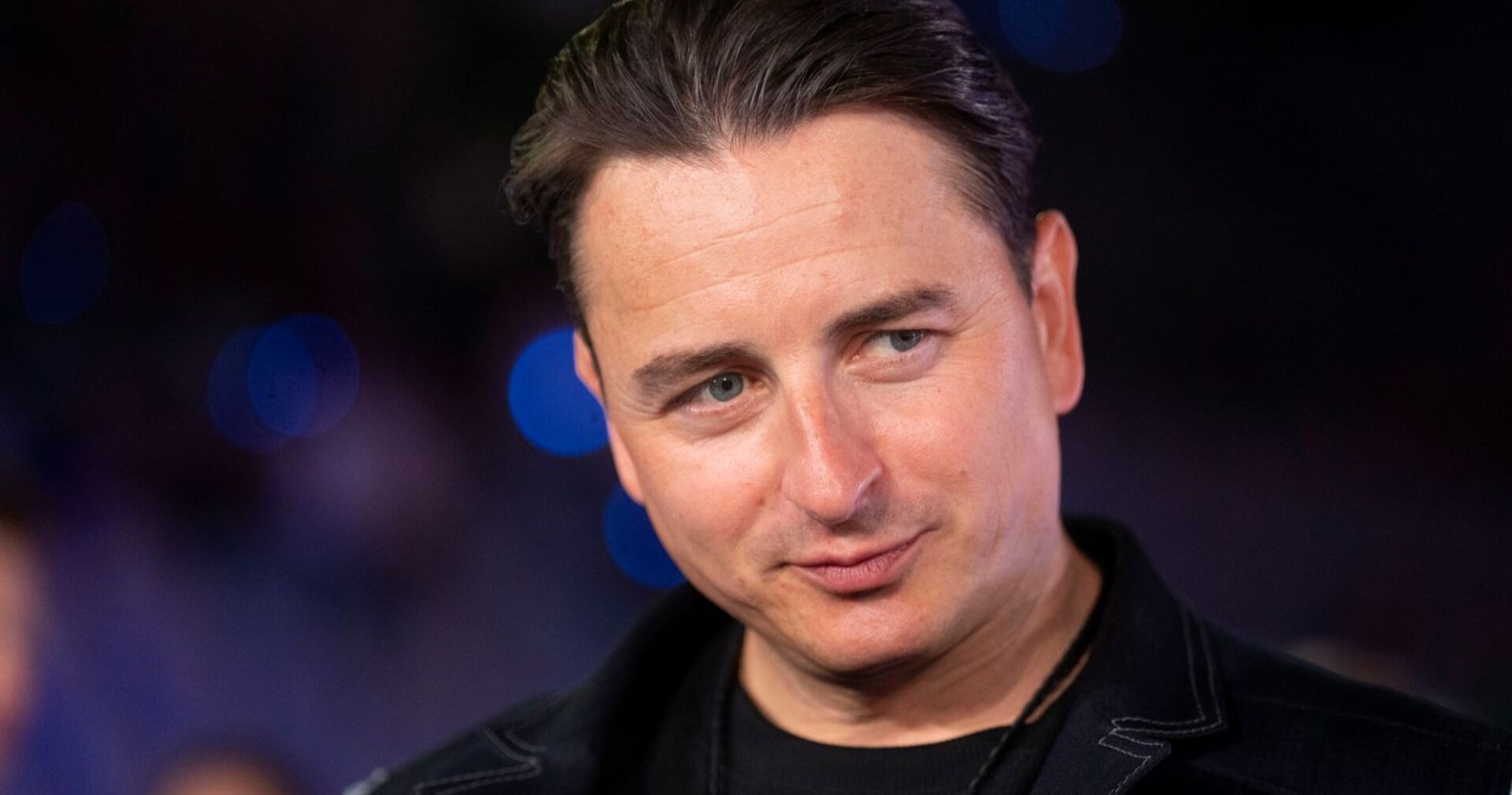 Andreas Gabalier mit ernstem Blick bei einem öffentlichen Auftritt, im Hintergrund unscharfe Lichter.