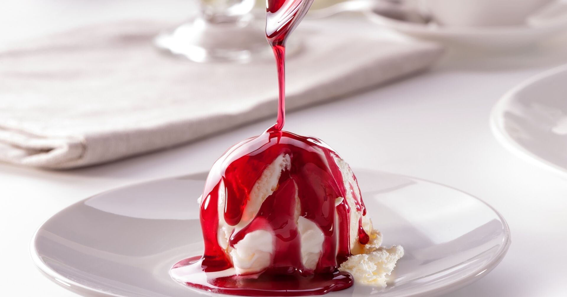 Kugel Vanilleeis auf Teller mit roter Fruchtsoße garniert