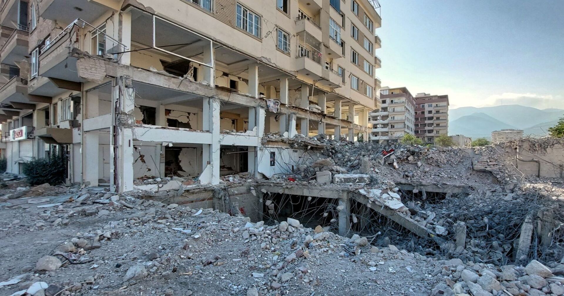 Teilweise eingestürztes mehrstöckiges Wohnhaus mit freiliegenden Stahlträgern und Trümmern im Vordergrund:  Nurdagi, Tuerkei, TUR - Zerstoerte Hochhaeuser im Erdbebengebiet Region Gaziantep