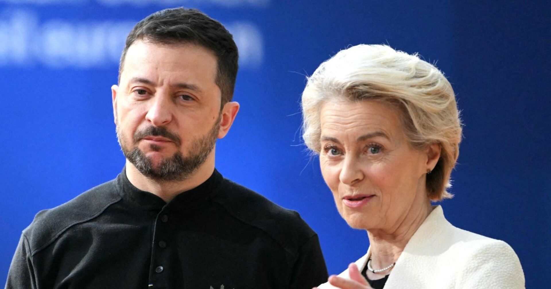 Der ukrainische Präsident Wolodymyr Selenskyj steht neben EU-Kommissionspräsidentin Ursula von der Leyen vor blauem Hintergrund. Beide blicken ernst, von der Leyen spricht mit leicht erhobener Handgeste.