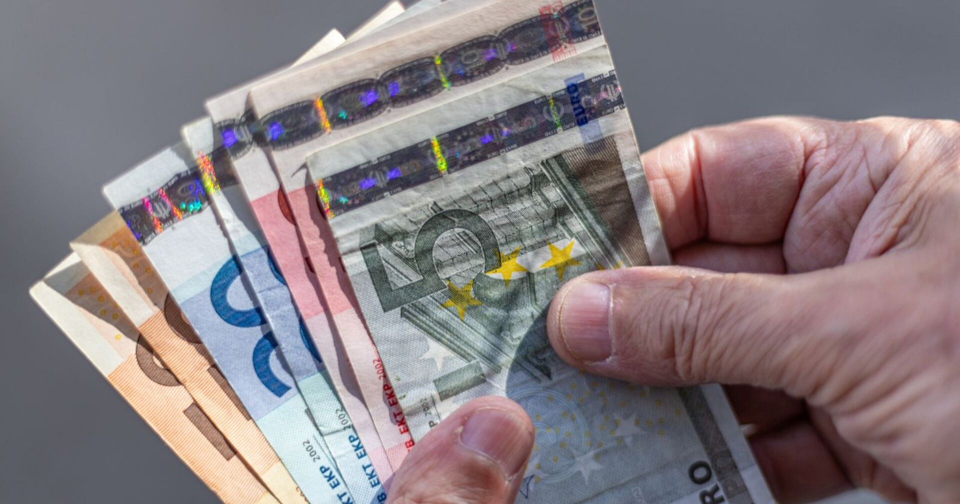 Alt-Text: Hände einer älteren Person halten mehrere Euro-Banknoten; symbolisch für Pensionen, Geldwert und soziale Absicherung im Alter.