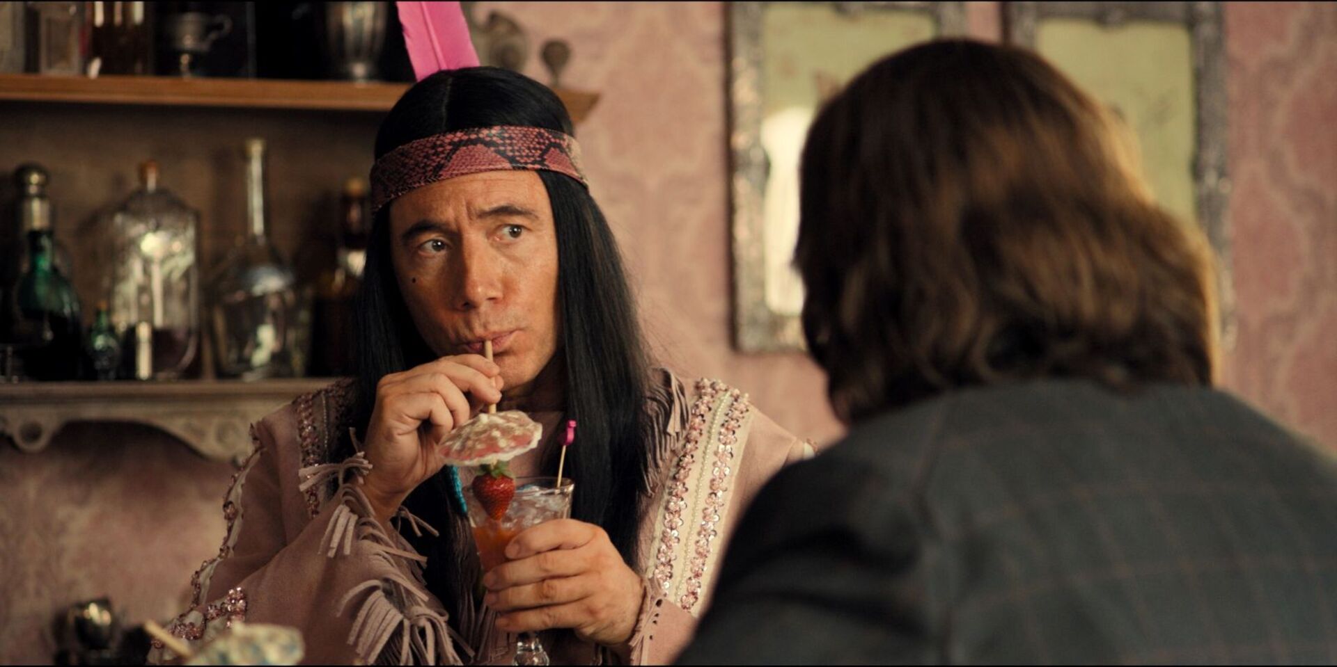 Figur Winnetouch (Michael Bully Herbig) sitzt in einem rosa Salon und trinkt einen Cocktail mit Erdbeere und Papierschirmchen.