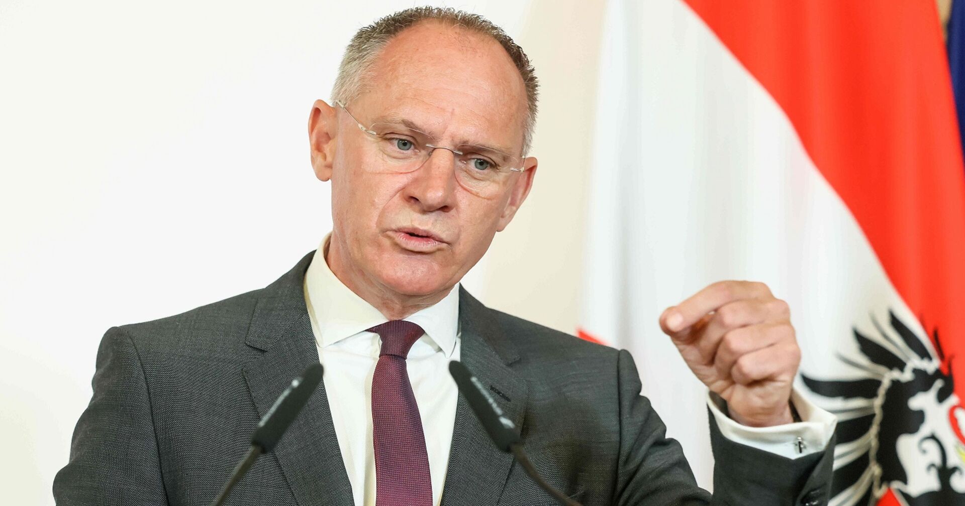 Gerhard Karner, österreichischer Innenminister, spricht bei einer Pressekonferenz vor Mikrofonen, im Hintergrund eine österreichische Fahne.