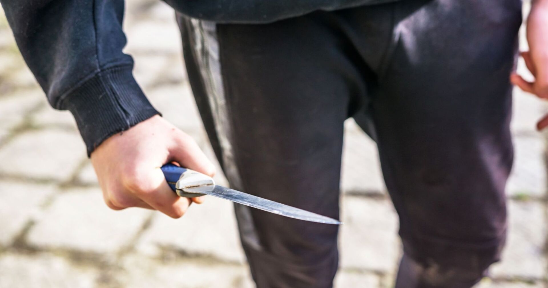 Mann im Jogginganzug, der am Tag auf der Straße ein Küchenmesser in seiner Hand hält