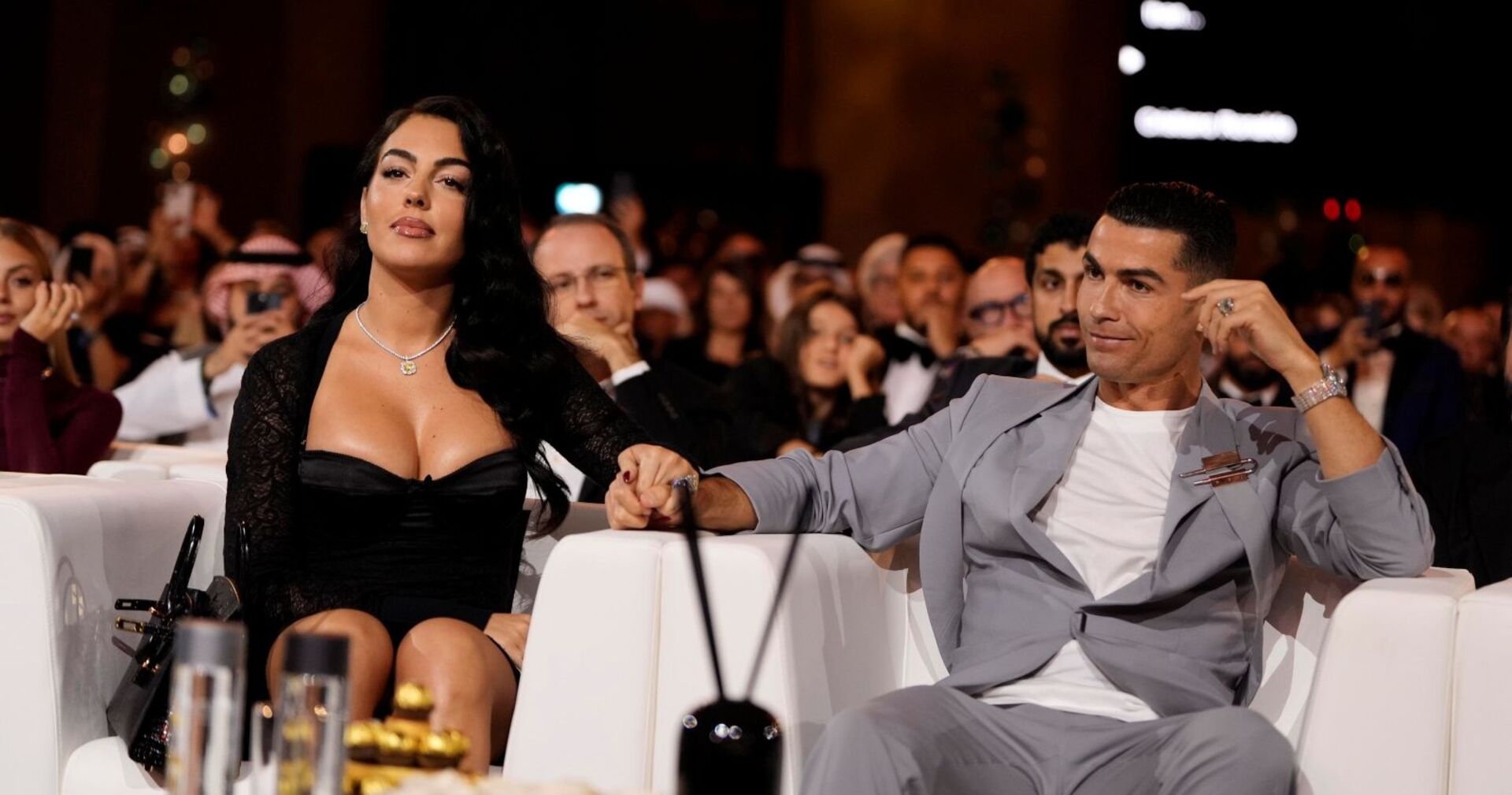 Cristiano Ronaldo und Georgina Rodríguez sitzen bei einer Gala nebeneinander, halten Händchen und präsentieren den funkelnden Verlobungsring.