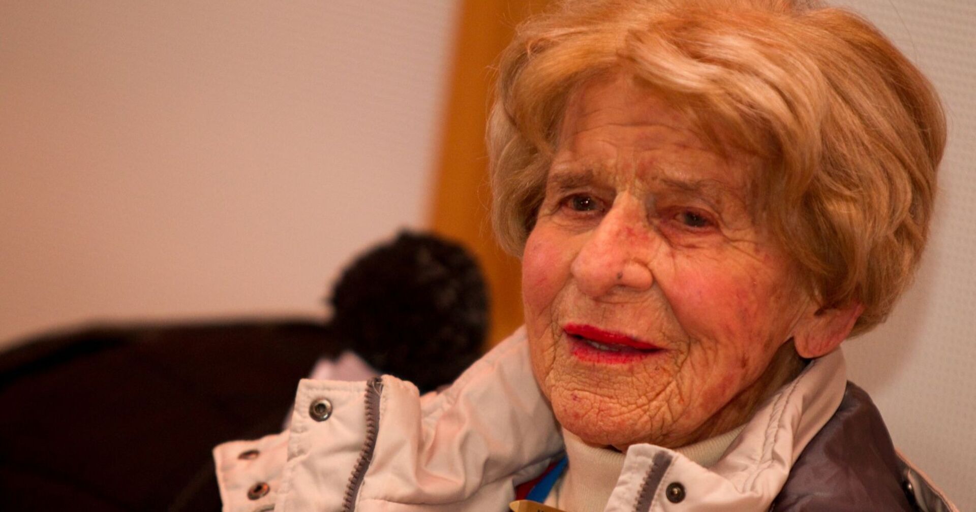 Porträt der betagten Anneliese Schuh-Proxauf mit hellbraunem Haar und Winterjacke, aufgenommen in einem Innenraum.