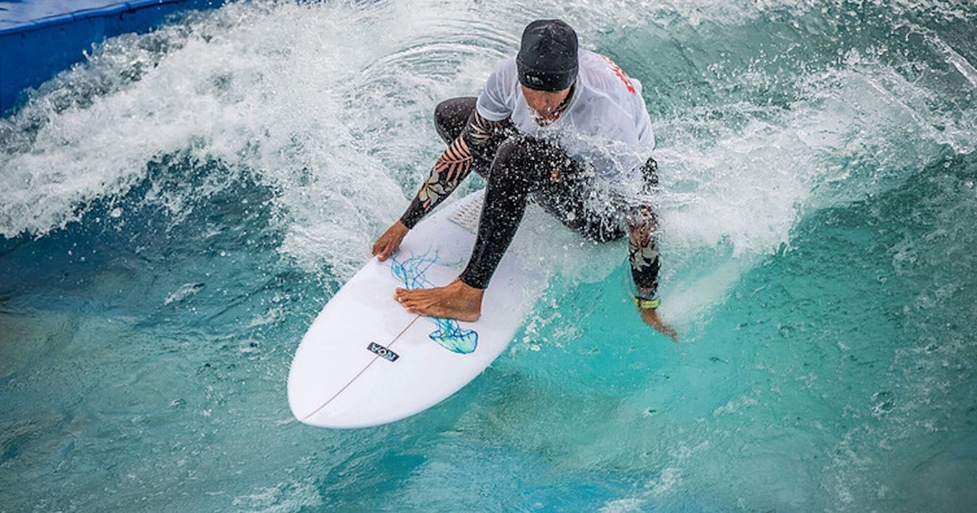Surfer im schwarzen Neoprenanzug, weißem Shirt und schwarzer Haube reitet die Welle