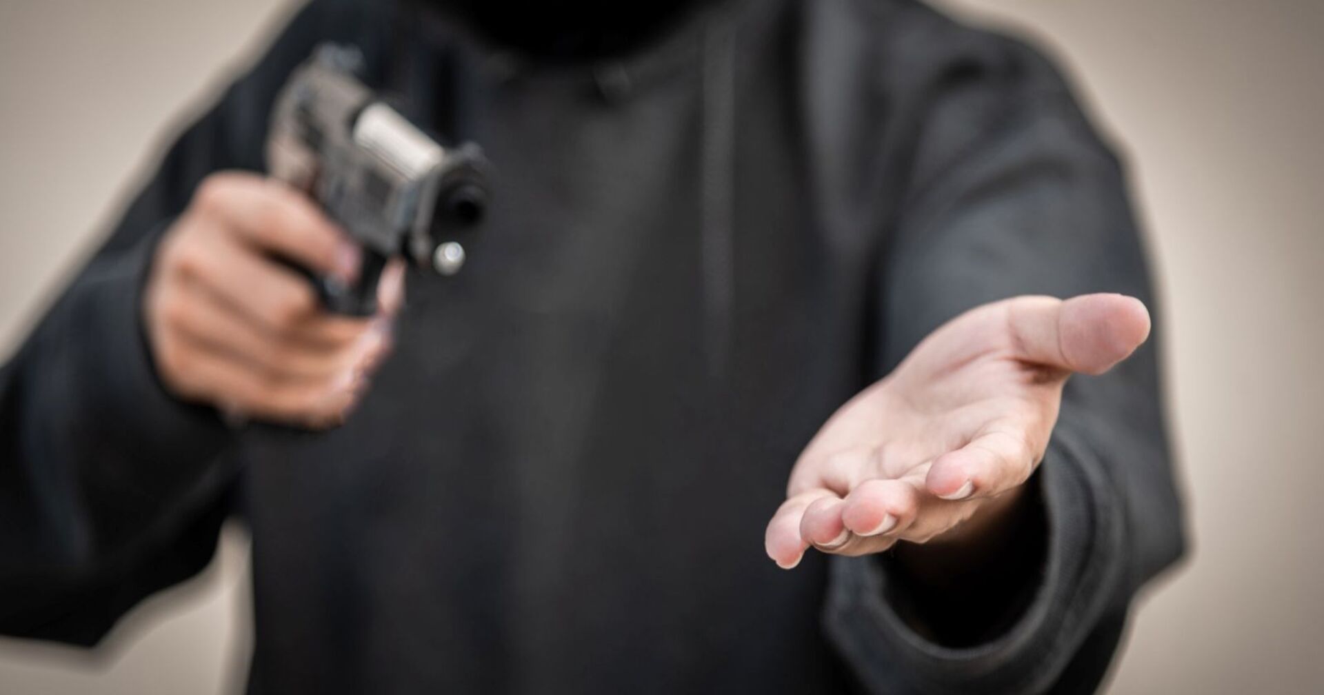 Mann in schwarzem Hoodie hält seine linke Hand auf, in der anderen Hand hält er eine Handfeuerwaffe