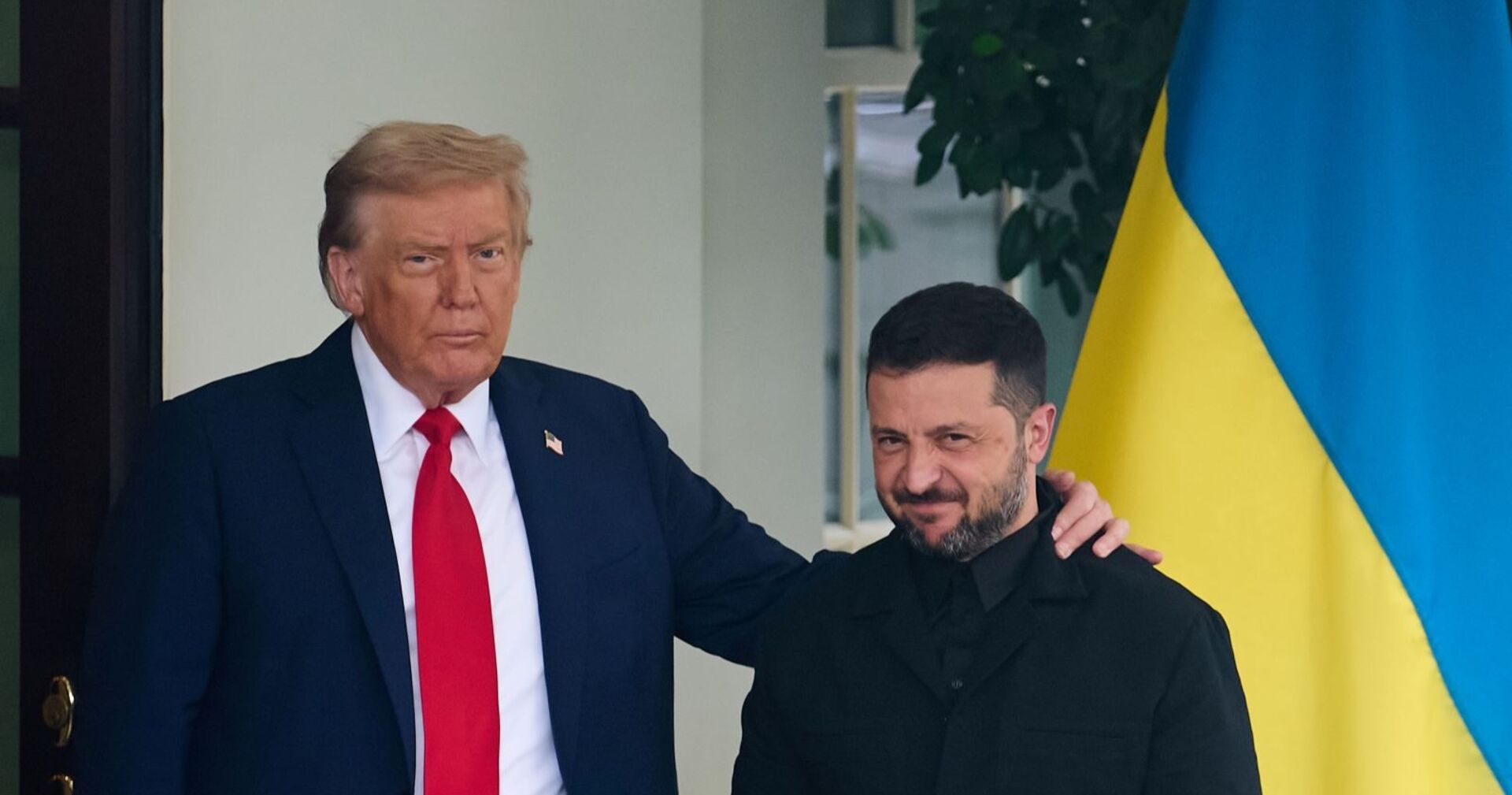 Donald Trump legt in Washington den Arm um Wolodymyr Selenskyj, daneben eine ukrainische Fahne.