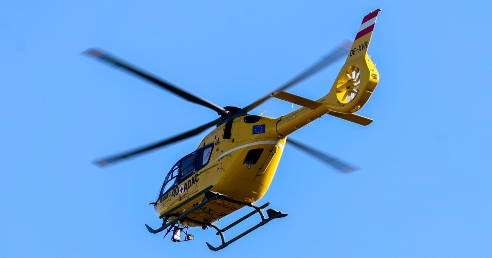 Gelber Notarzthubschrauber des ÖAMTC im Flug vor blauem Himmel, aufgenommen während eines Rettungseinsatzes.