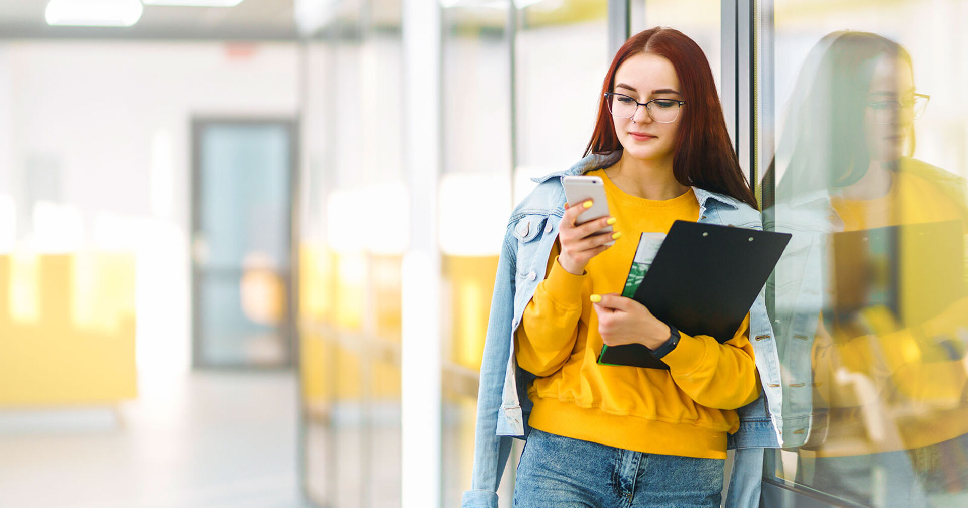 Junge Frau lehnt mit ihren Unterlagen in der Hand gegen eine Glastür | Credit: Adobe Stock