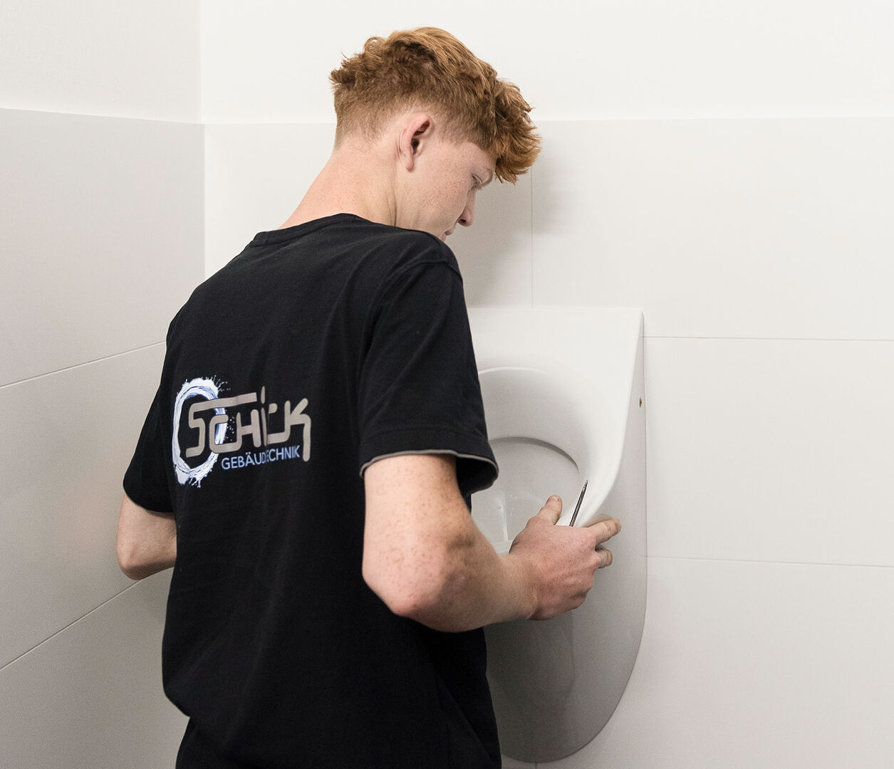 Junger Installateur montiert ein Pissoir an der Wand | Credit: Schick Gebäudetechnik