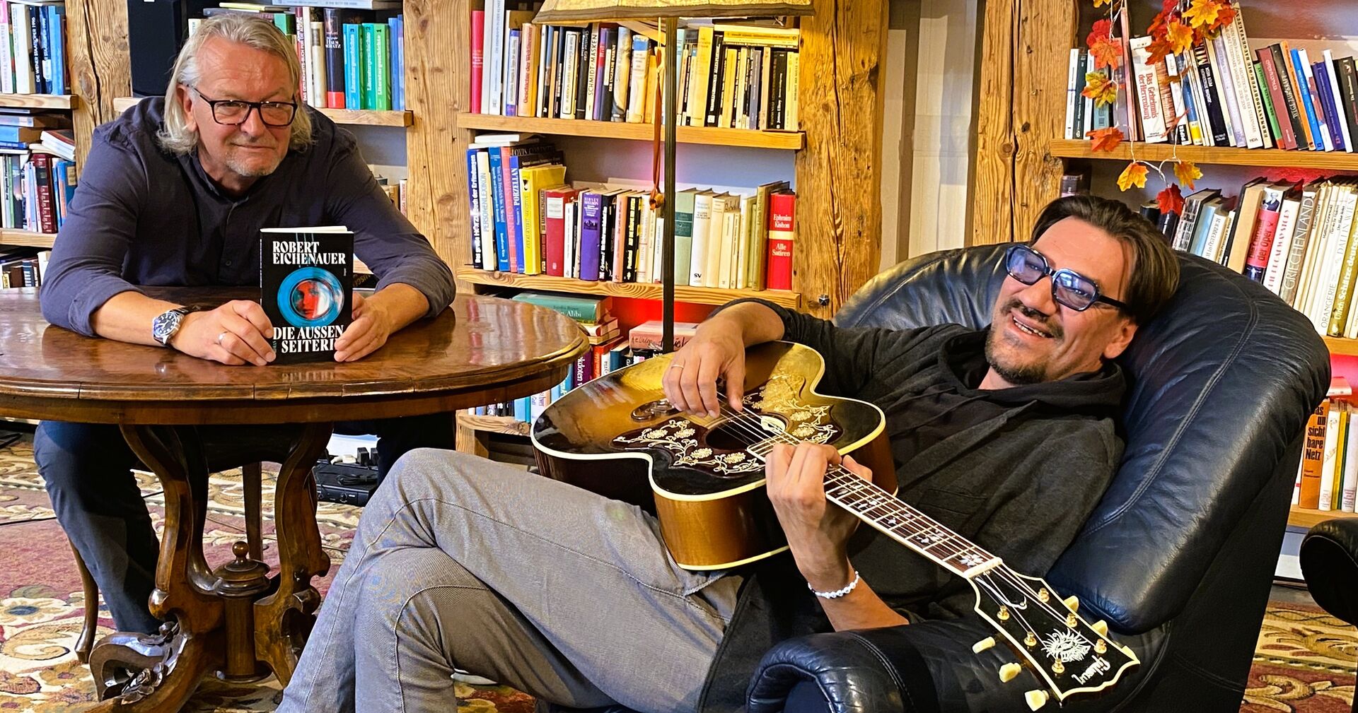 Zwei Männer mit einer Gitarre und einem Buch in der Hand.