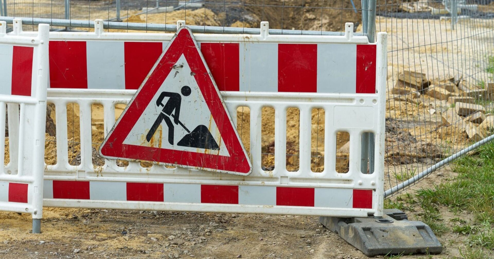 Absperrung einer Baustelle ein dreickiges Baustellenwarnschild ist auf einem Zaun angebracht