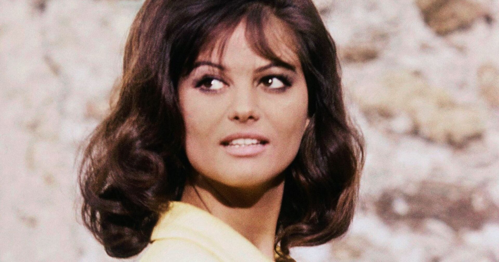 Porträt der jungen Claudia Cardinale mit braunen Haaren und gelbem Kleid, aufgenommen in den 1960er-Jahren.