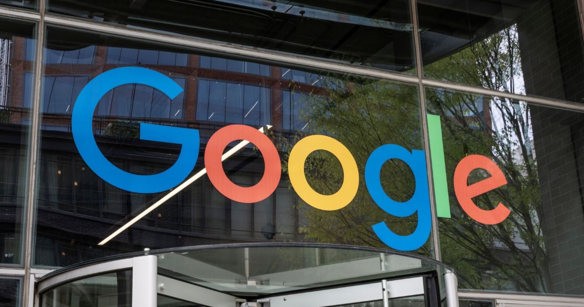 Großes, buntes Google-Logo an der Glasfassade eines Bürogebäudes, aufgenommen von außen mit Blick auf den Eingangsbereich.