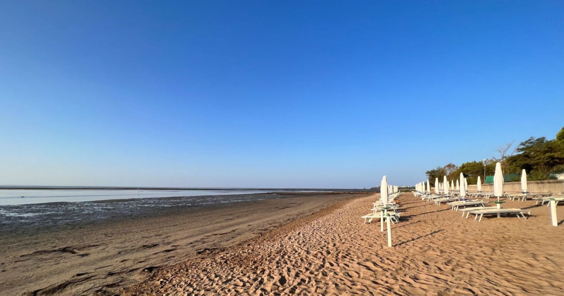 Leerer Sandstrand mit geschlossenen Sonnenschirmen und Liegen am Meer in Grado, Italien – Ort eines tödlichen Badeunfalls mit einem vierjährigen Kind.