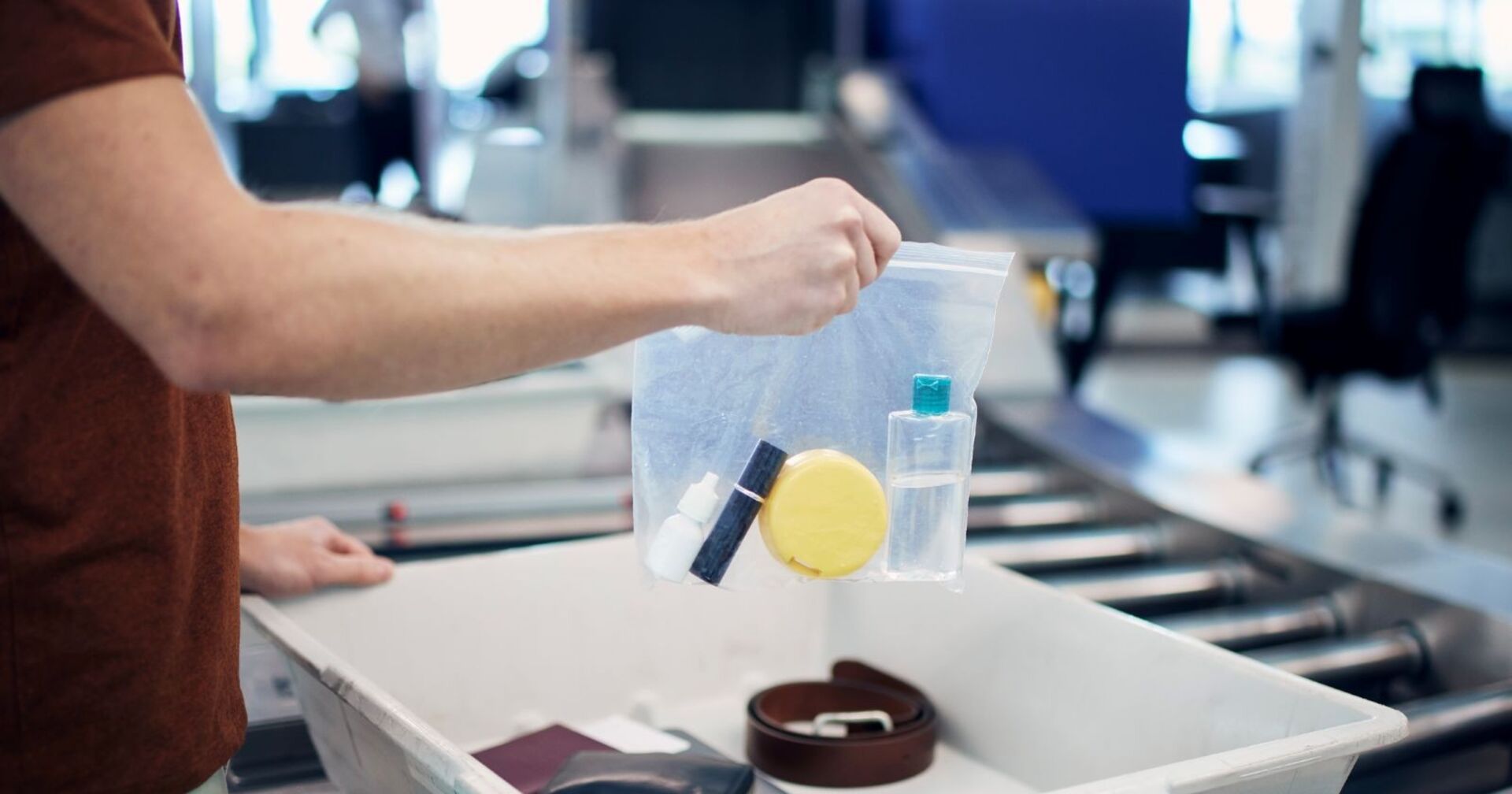 icherheitskontrolle am Flughafen vor dem Flug. Passagier hält Plastiktüte mit Flüssigkeiten über dem Behälter mit Laptop und persönlichen Gegenständen