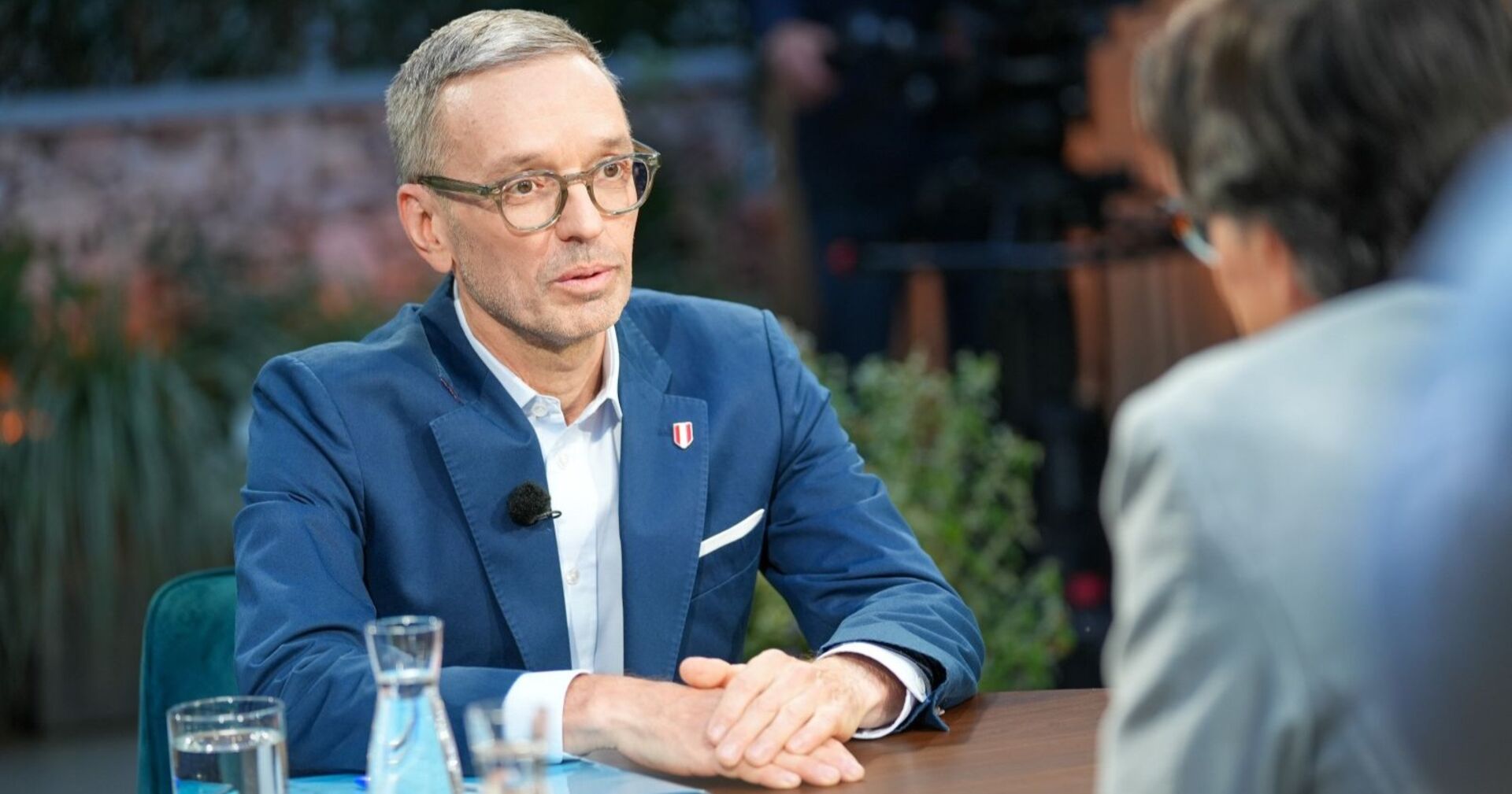 Herbert Kickl sitzt im ORF-Sommergespräch an einem Tisch, trägt Brille und blauen Anzug, spricht mit Moderator Klaus Webhofer.