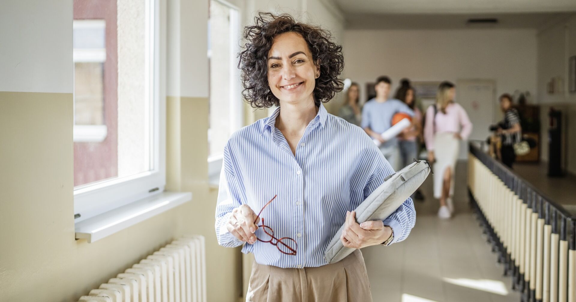 Eine Lehrerin steht am Gang einer Schule und lächelt
