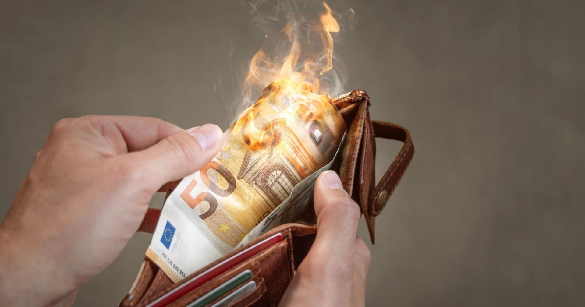 Eine Hand hält eine Geldbörse, aus der ein brennender 50-Euro-Schein ragt – Symbol für die steigende Inflation und Kaufkraftverluste.