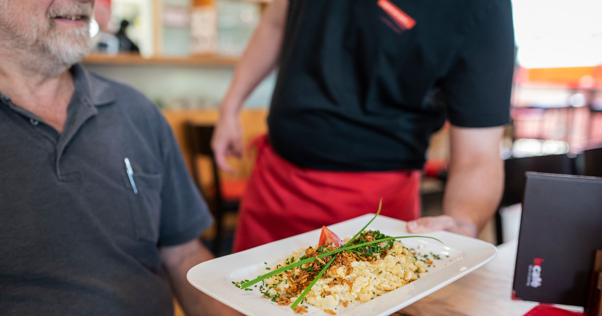 Kellner serviert Mann seine Bestellung | Credit: Jugend am Werk Steiermark/ Miriam Raneburger
