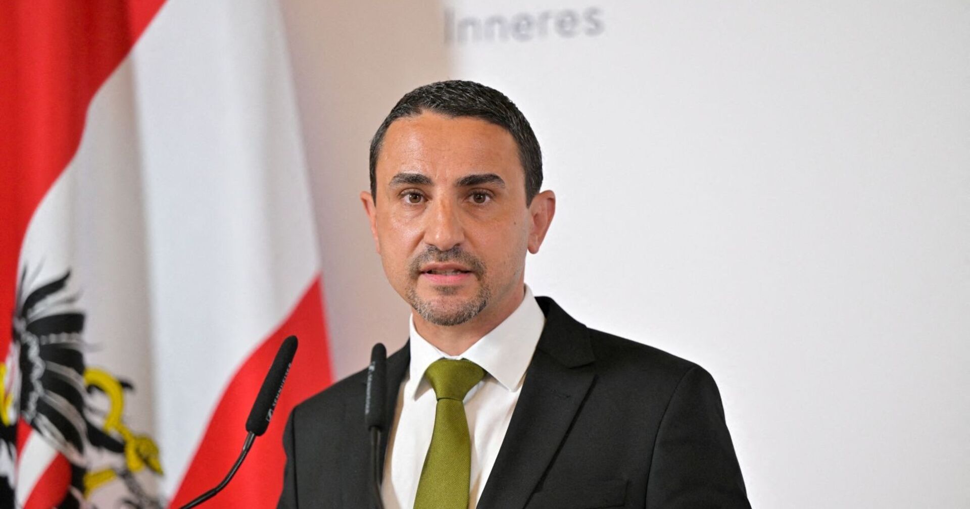 Omar Haijawi-Pirchner im Anzug bei einer Pressekonferenz vor österreichischer Fahne.