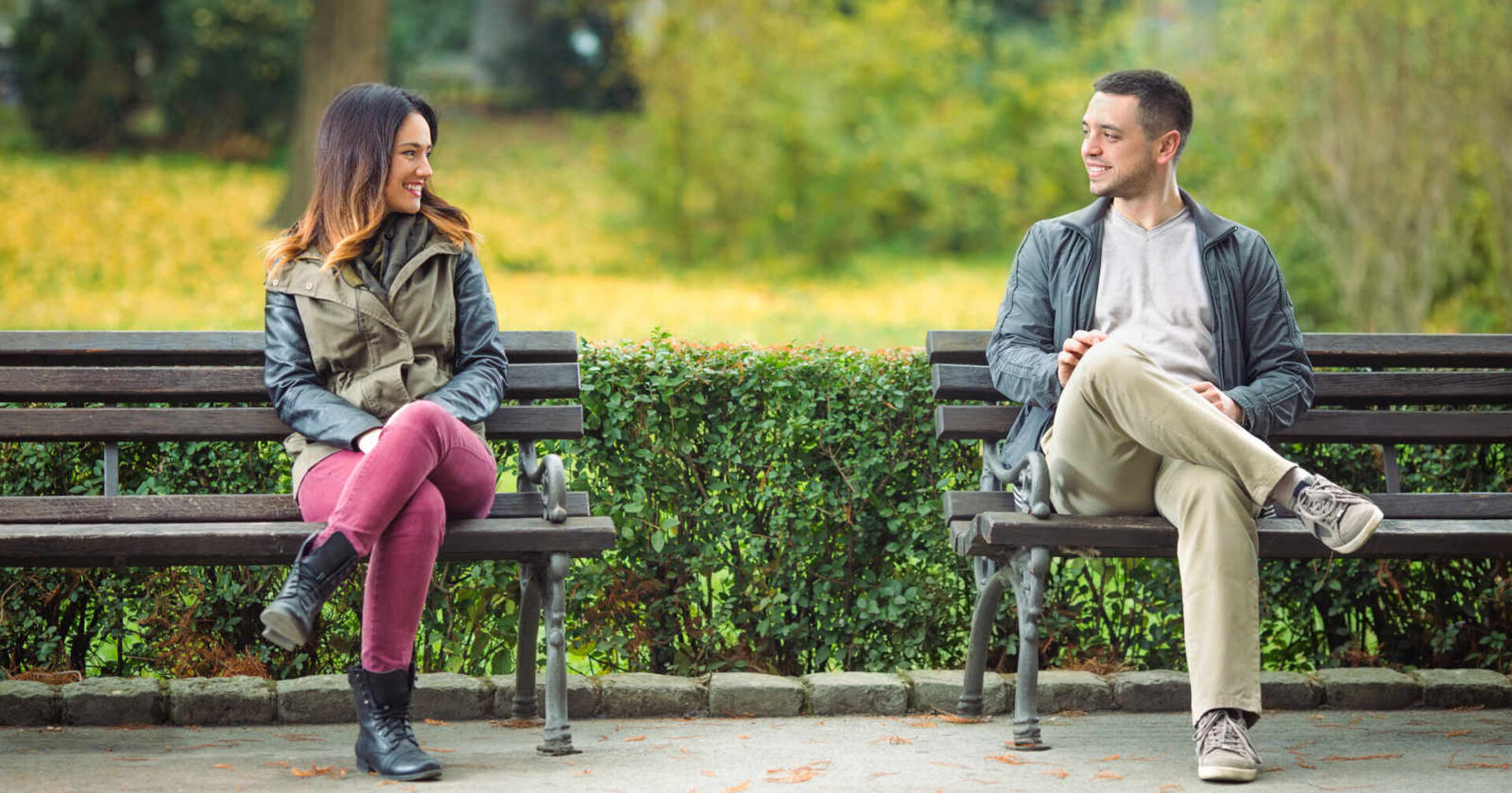 Zwei Menschen sitzen auf Parkbänken und lächeln sich an
