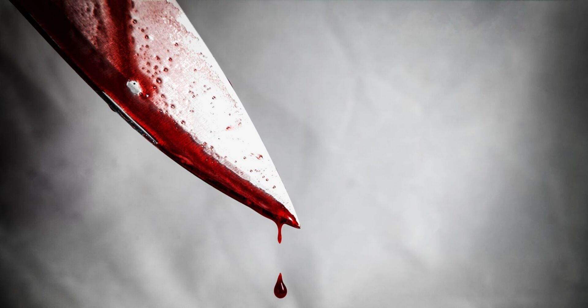 Naheaufnahme eines mit Blut tropfenden Messers vor grauem Hintergrund