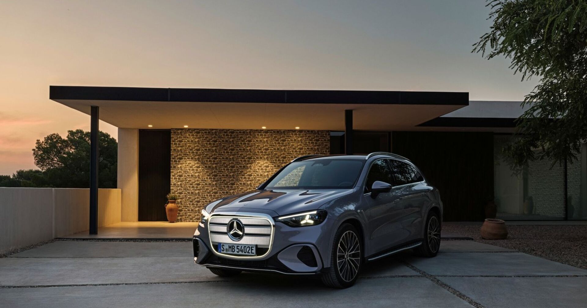 Ein Mercedes GLS parkt vor einem eleganten Haus. Die Sonne geht im Hintergrund unter und lässt das silberne Auto glänzen.