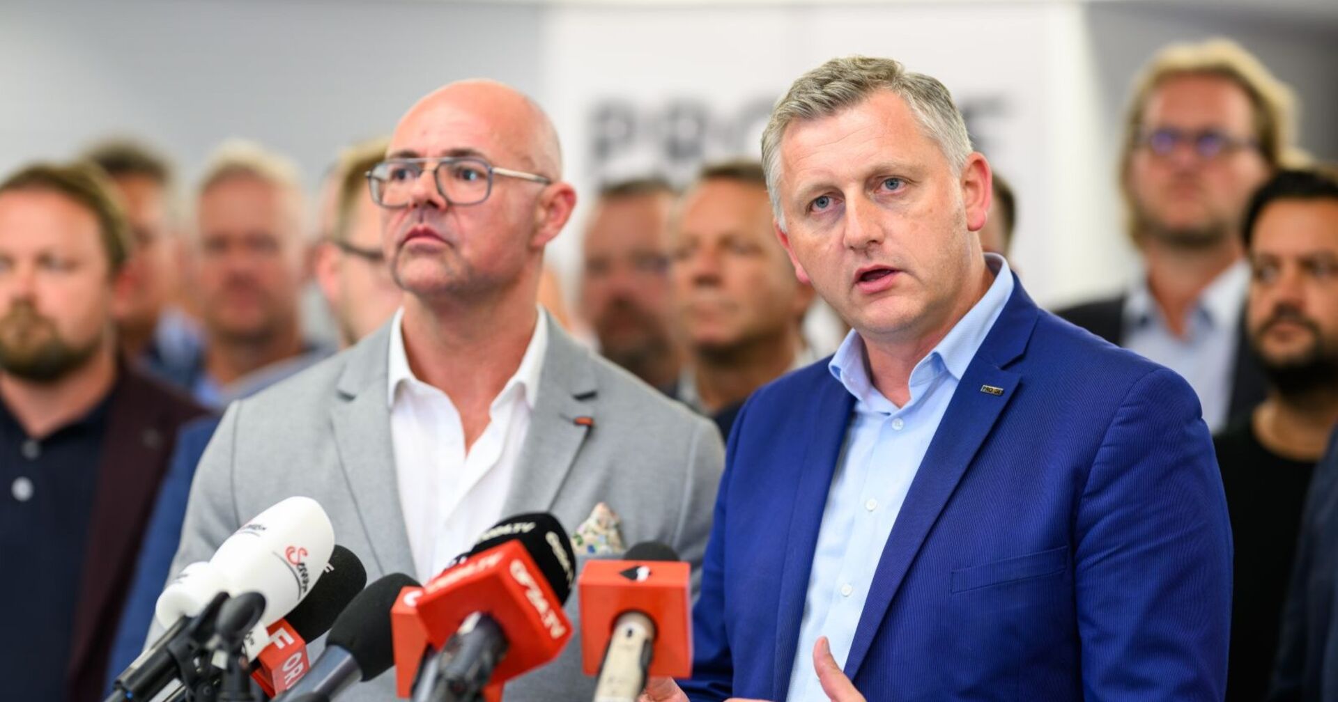 Die zwei Gewerkschaftstsverhandler der Metallbranche,  Mario Ferrari (GPA) und Reinhold Binder (PRO-GE), stehen bei einer Pressekonferenz vor Mikrofonen und sprechen über den erreichten Kollektivvertragsabschluss.