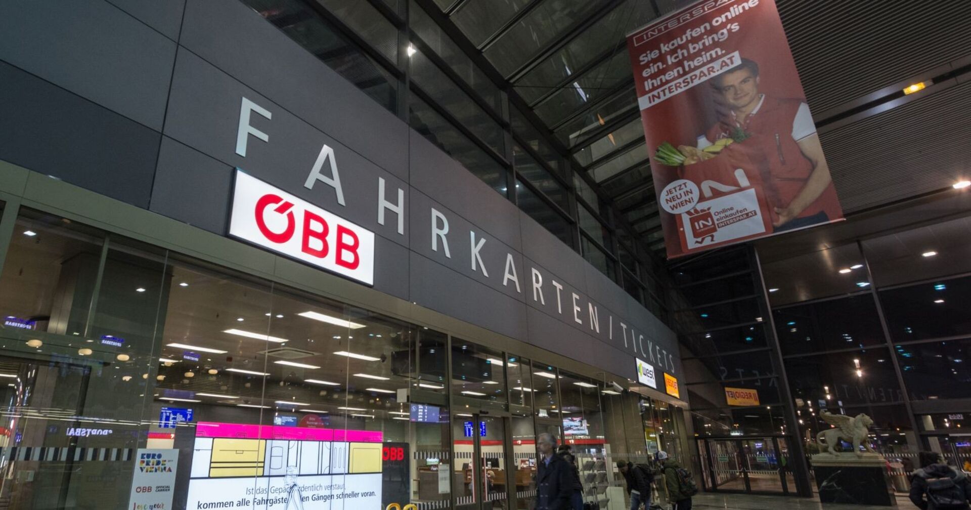 Eingang zum Fahrkartencenter der ÖBB im Wiener Hauptbahnhof mit leuchtendem ÖBB-Logo am Abend