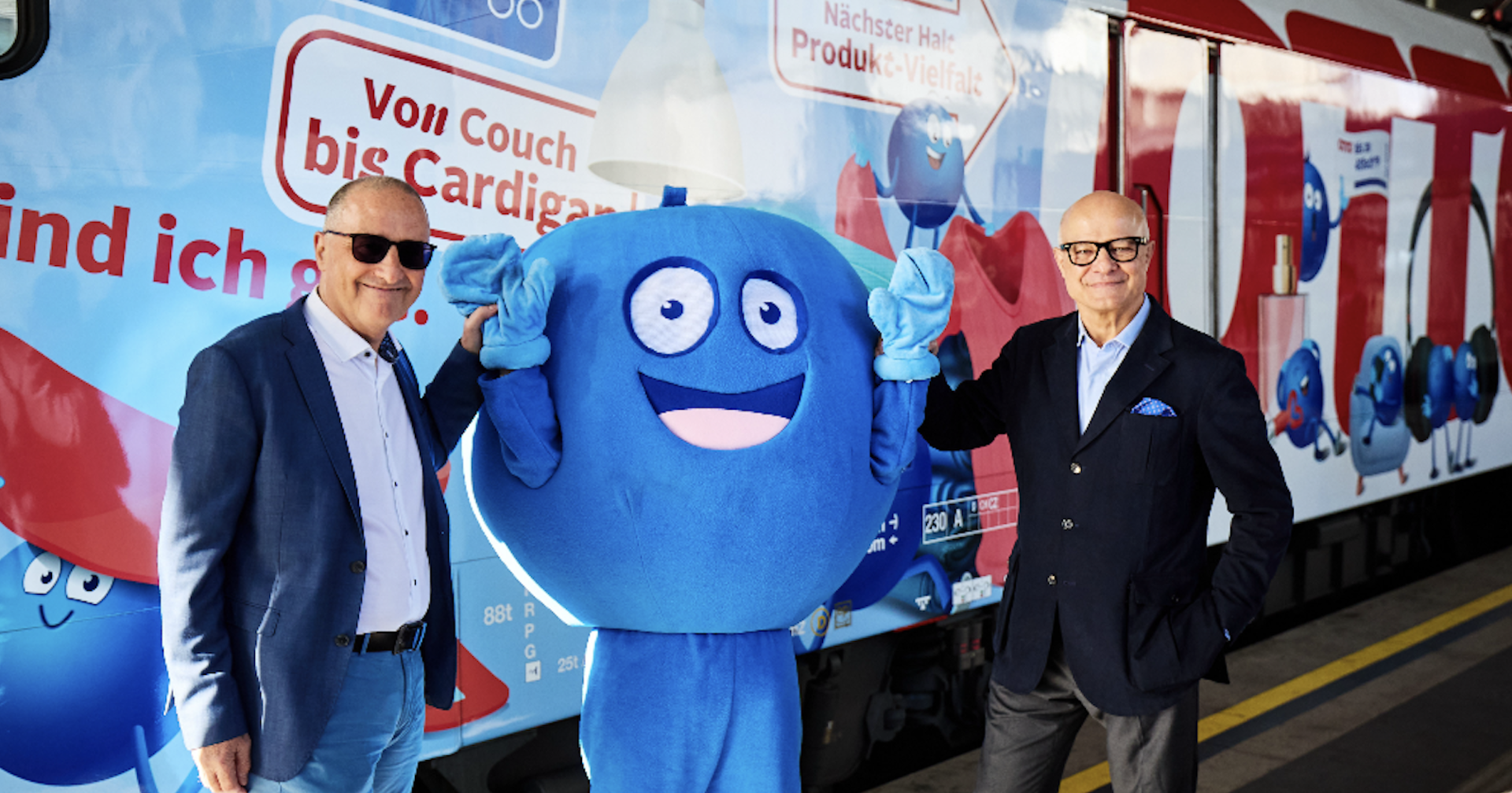 Zwei Geschäftsführer mit Maskottchen vor der neuen Werbelok