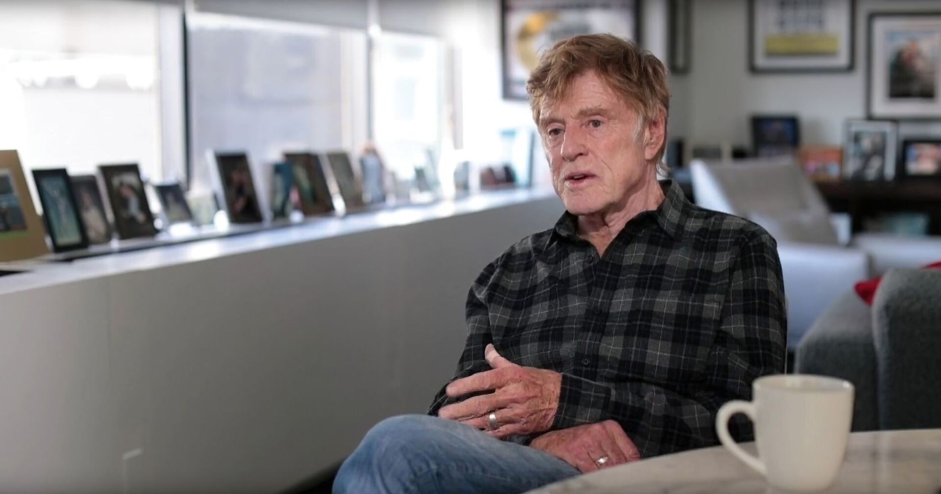 Robert Redford im Flanellhemd sitzend mit einer Tasse Kaffee