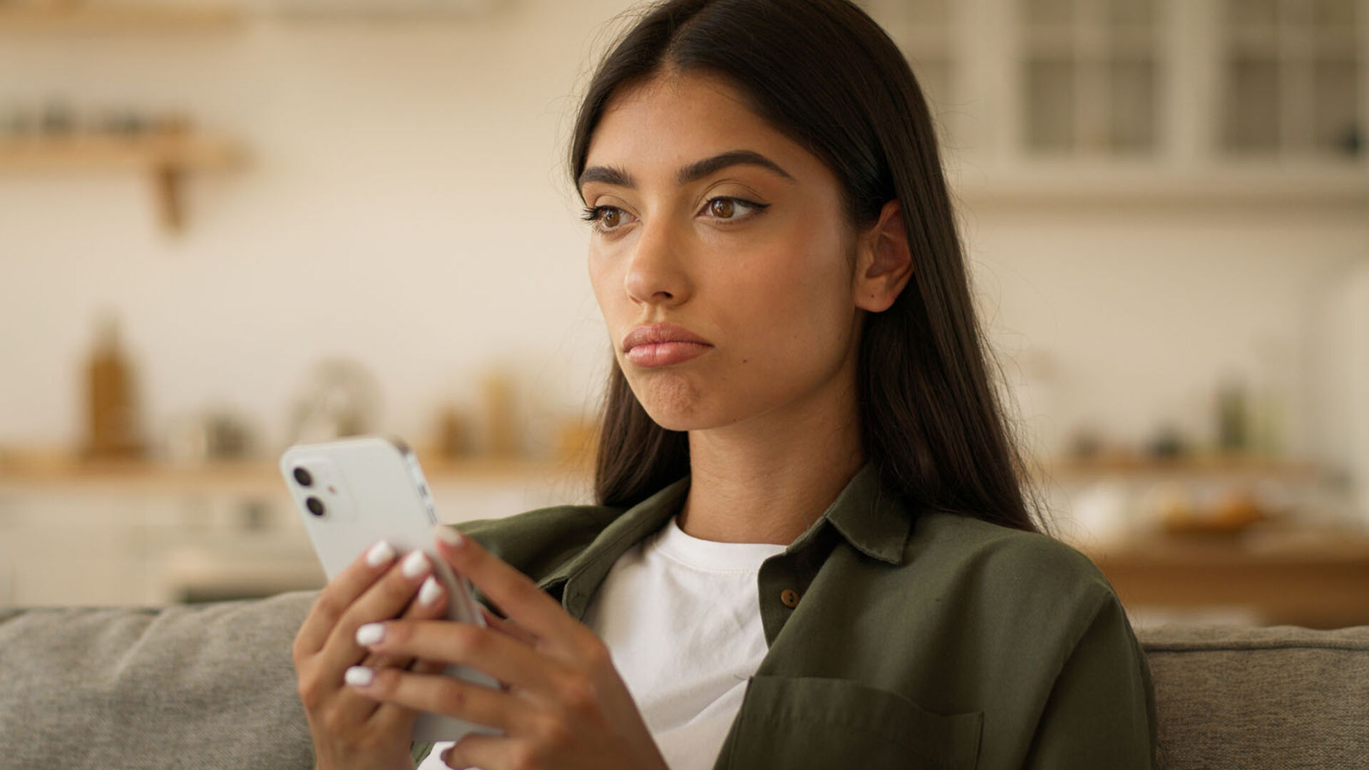 Frau sitzt mit Smartphone auf der Couch | Credit: iStock.com/Yuliia Kaveshnikova