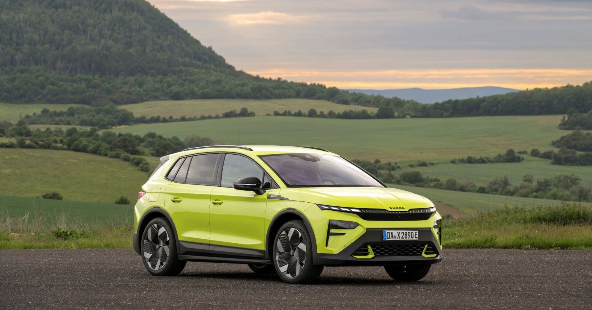 Ein mambagrüner Skoda Elroq RS parkt vor Wiesen und Hecken. Im Hintergrund ist ein bewaldeter Berg zu sehen.