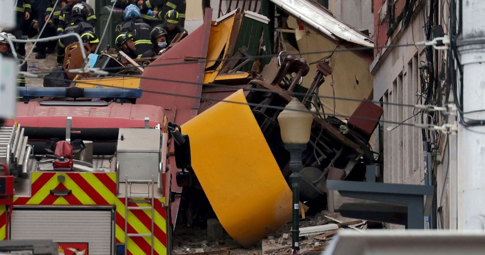 Zerstörter gelber Waggon der Standseilbahn „Elevador da Glória“ nach dem schweren Unfall in Lissabon, umgeben von Feuerwehrleuten und Rettungskräften.