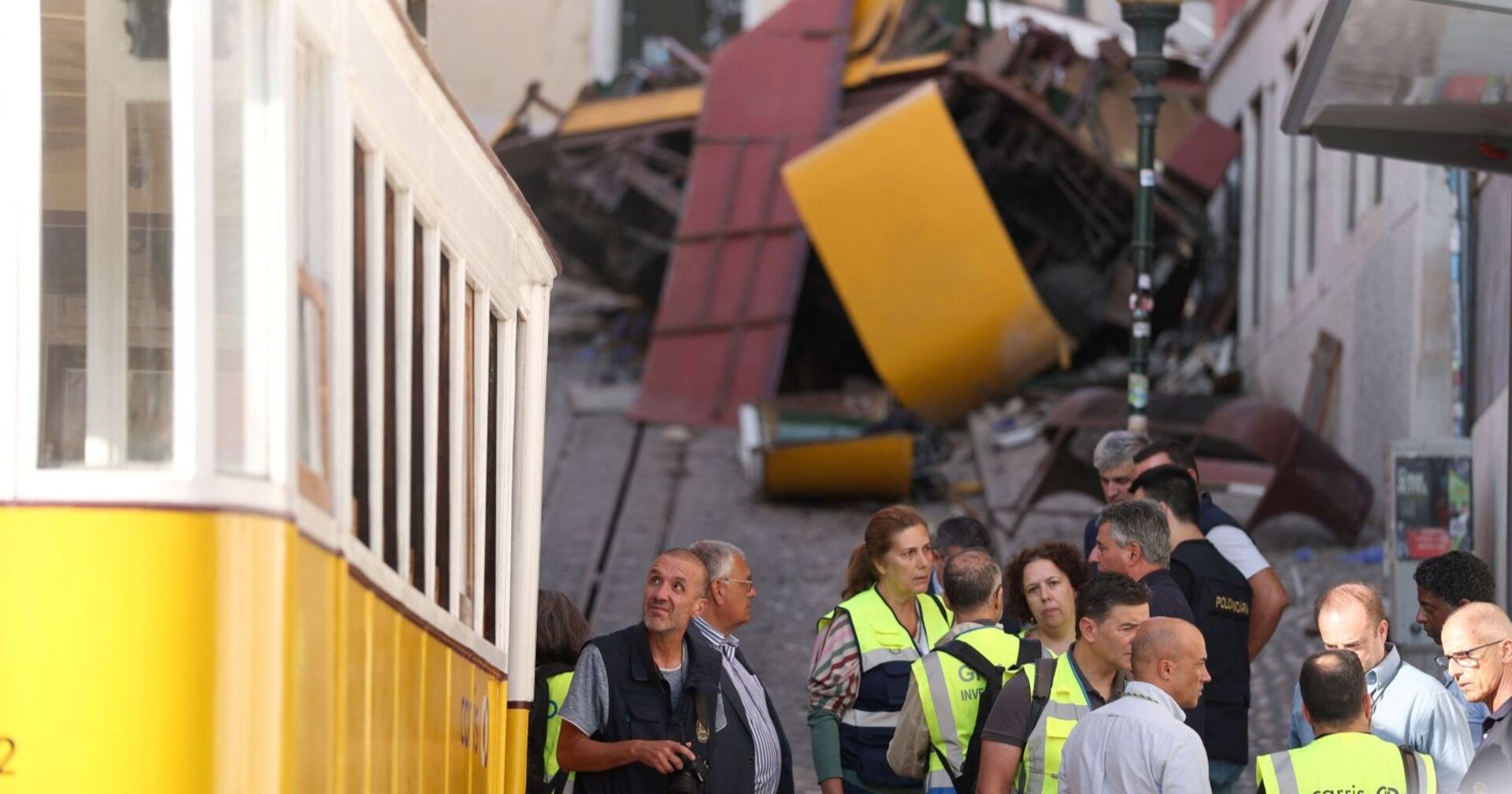Ermittler und Einsatzkräfte stehen vor den Trümmern des entgleisten „Elevador da Glória“ in Lissabon – im Hintergrund der zerstörte gelbe Waggon.